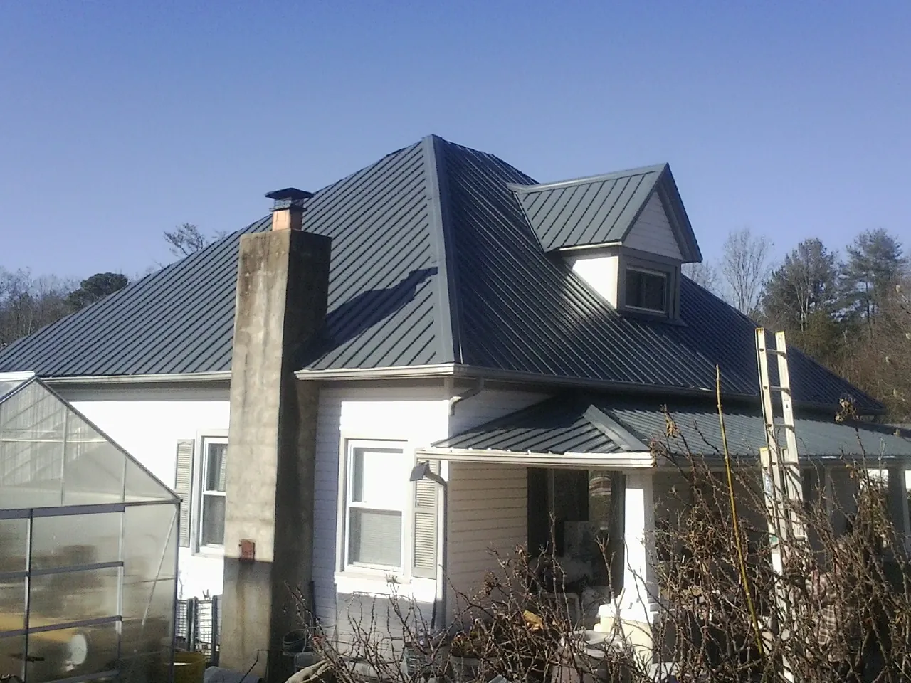 Dark blue standing seam metal roof on a white farmhouse with dormer — Slate & Tile Roof Repair by Roofing Brothers in Massey