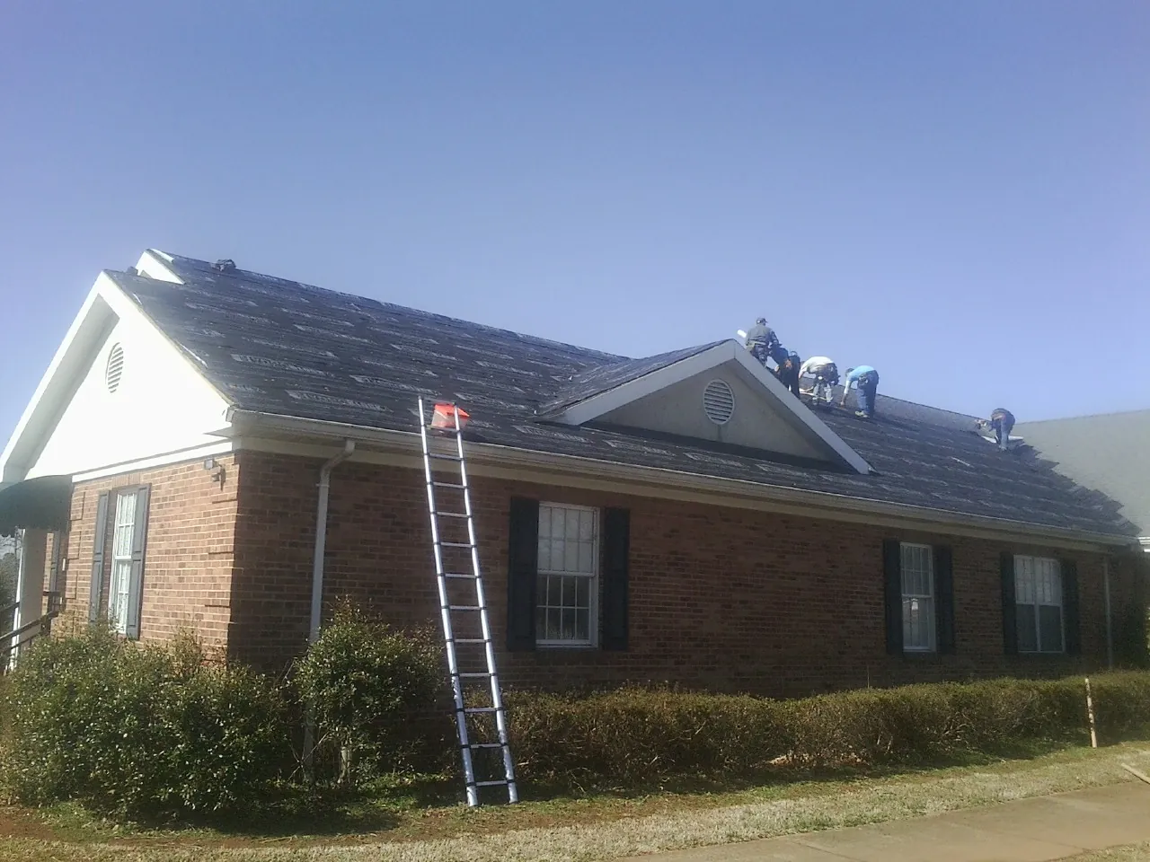Crew tearing shingles off a brick ranch roof with a ladder set — Emergency Roof Repair work by our crew in Massey
