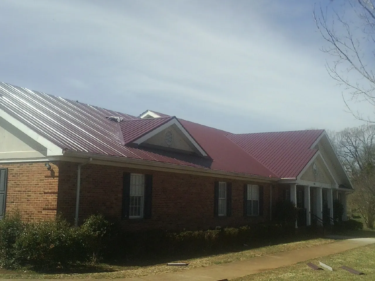 Red metal roof with gabled entries on a long brick building, from a Hail Damage Roof Repair job in Massey