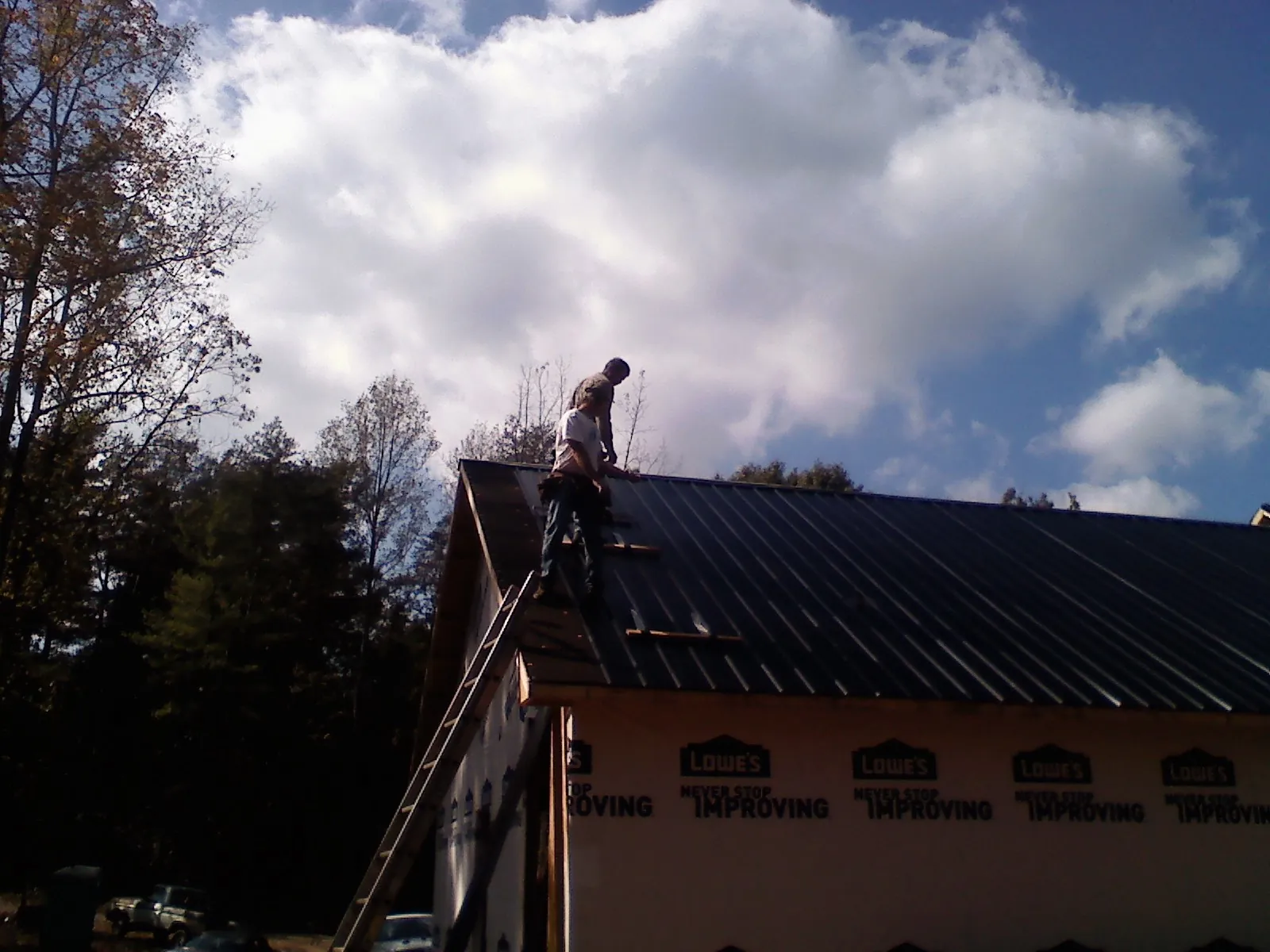 Roofer fastening dark metal panels high against a cloudy sky, from a Roof Inspection job in Massey