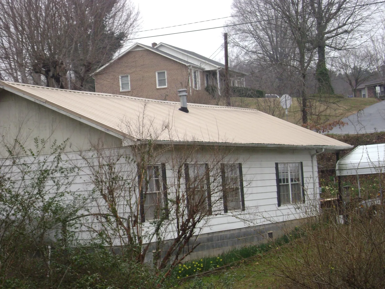 Tan metal roof on a white sided house set into a hillside — Commercial Roofing by Roofing Brothers in Massey